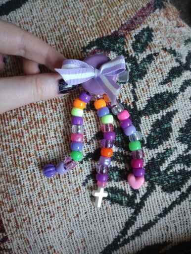 A DIY hair clip with a small bow and three strands of pony beads dangling from it. Purple with small hints of orange, green, and pink.