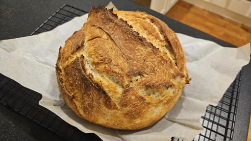 Round artisan bread loaf on a piece of baking paper on a cooking rack