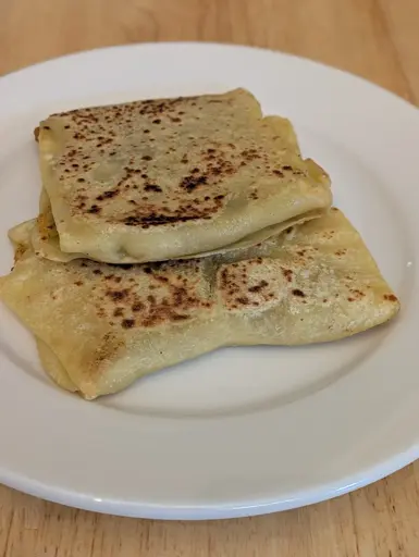two semolina flour based stuffed flatbreads in a square or rectangular shape sitting on a white plate.